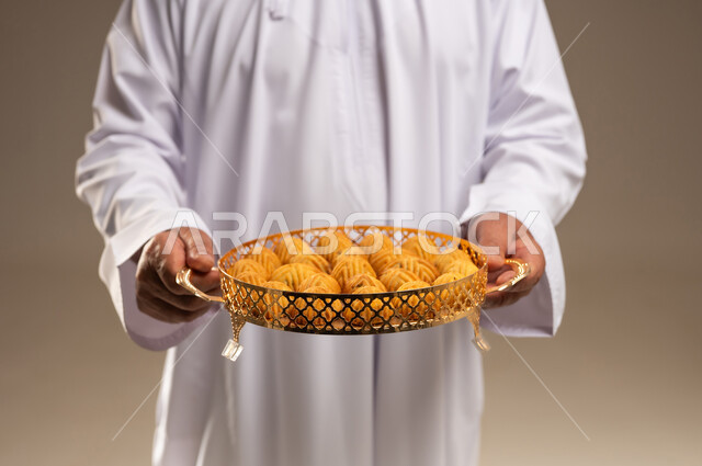 رجل عربي يحمل صينية ذهبية مليئة بالمعمول في الاستوديو