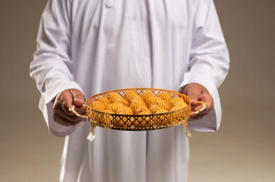 رجل عربي يحمل صينية ذهبية مليئة بالمعمول في الاستوديو