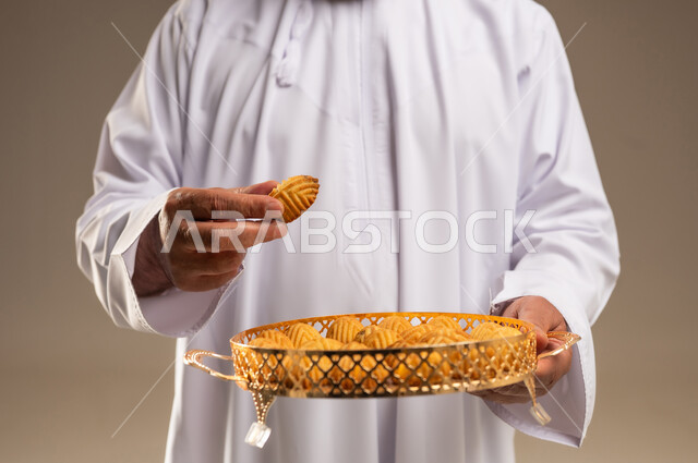 رجل سعودي بالزي التقليدي يحمل صينية من معمول العيد