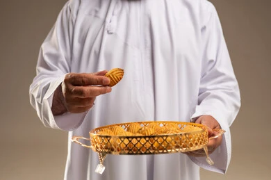 رجل سعودي بالزي التقليدي يحمل صينية من معمول العيد