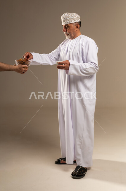 رجل عماني بالزي التقليدي يتناول التمر والقهوة