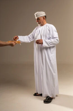 رجل عُماني بالزي التقليدي يتناول القهوة والتمر
