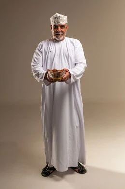 رجل عماني بملابس تقليدية يحمل وعاء من التمر في استوديو