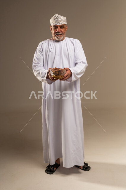 رجل عماني بالزي التقليدي يحمل وعاء من التمر