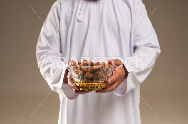 رجل عربي بالثوب الأبيض يحمل وعاء من التمر