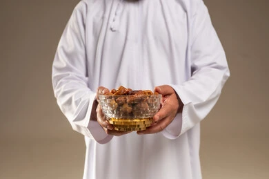 رجل عربي بالثوب الأبيض يحمل وعاء من التمر