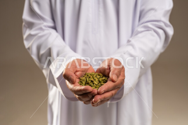 رجل عربي بالثوب الأبيض يحمل حبات الهيل الأخضر