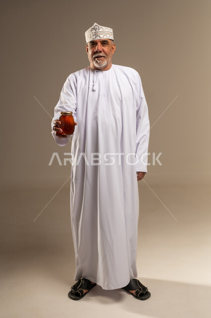 رجل عماني كبير السن يحمل برطمان عسل في الاستوديو