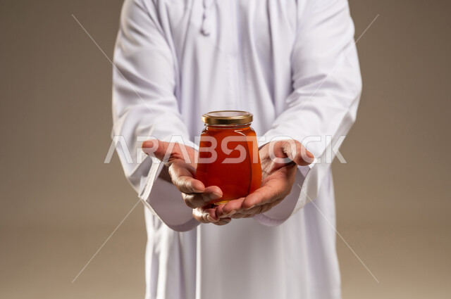 رجل سعودي يرتدي الثوب يحمل جرة عسل طبيعي