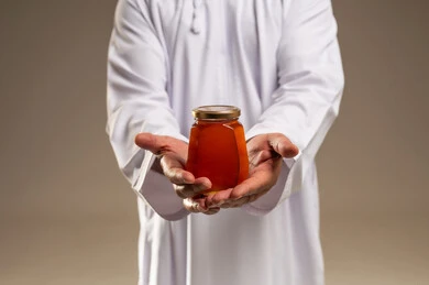 رجل سعودي يرتدي الثوب يحمل جرة عسل طبيعي