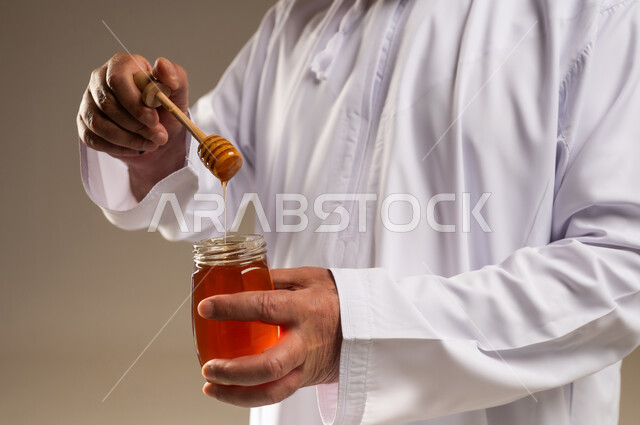 رجل سعودي بالثوب الأبيض يمسك مرطبان عسل