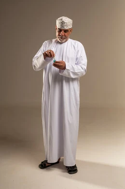 رجل عُماني بالزي التقليدي يفتح زجاجة عطر في استوديو