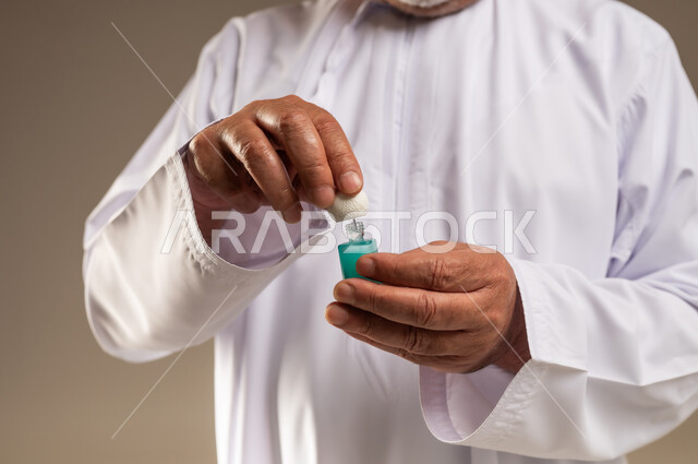 رجل عربي بالثوب الأبيض يمسك زجاجة عطر دهن العود