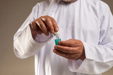 رجل عربي بالثوب الأبيض يمسك زجاجة عطر دهن العود