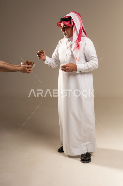 رجل سعودي بالزي التقليدي يتناول التمر والقهوة