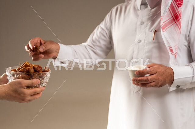 رجل سعودي يحمل فنجان قهوة عربية وتمر في استوديو