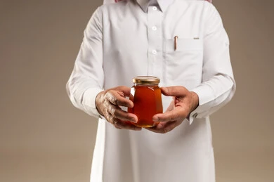 رجل سعودي يحمل جرة عسل طبيعي في خلفية استوديو بيج