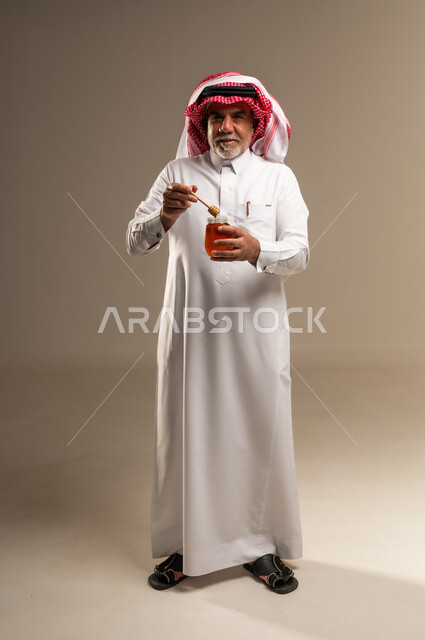 رجل سعودي مسن يحمل مرطبان عسل طبيعي في الاستوديو