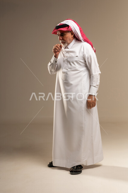 رجل سعودي مسن يسعل بالثوب التقليدي في استوديو