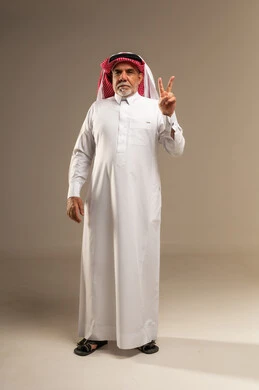 رجل سعودي مسن يؤدي إيماءة النصر في استوديو محايد