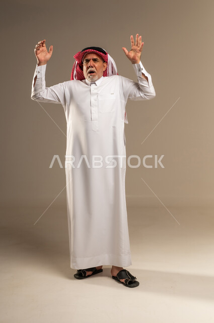 رجل سعودي مسن يرفع يديه في الاستوديو