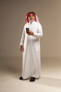 رجل سعودي مسن يحمل هاتفا ذكيا في الاستوديو