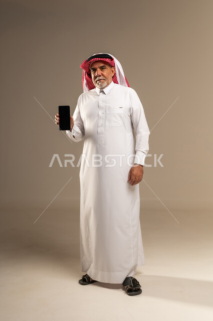 رجل سعودي مسن يحمل هاتف ذكي في الاستوديو