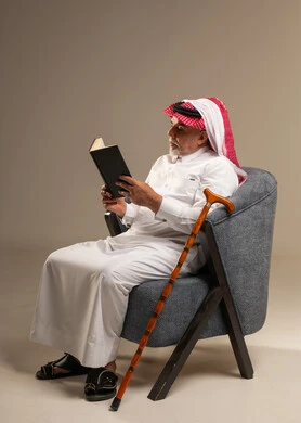 An elderly Saudi man in traditional attire is holding a book.