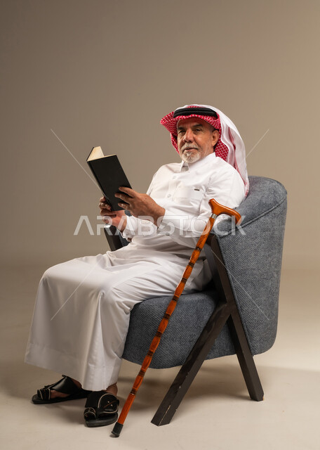 رجل سعودي مسن بالزي التقليدي يمسك كتاباً
