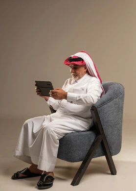 An elderly Saudi man is using a tablet in the studio.