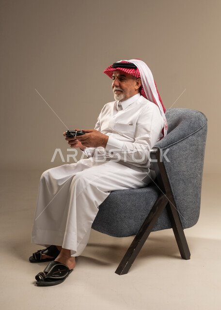 رجل سعودي مسن يمسك بجهاز تحكم ألعاب في الاستوديو