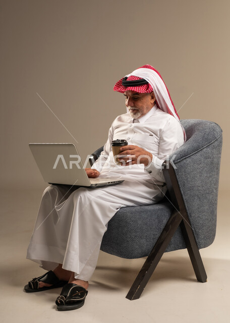 رجل سعودي يستخدم المحمول ويحمل كوب قهوة