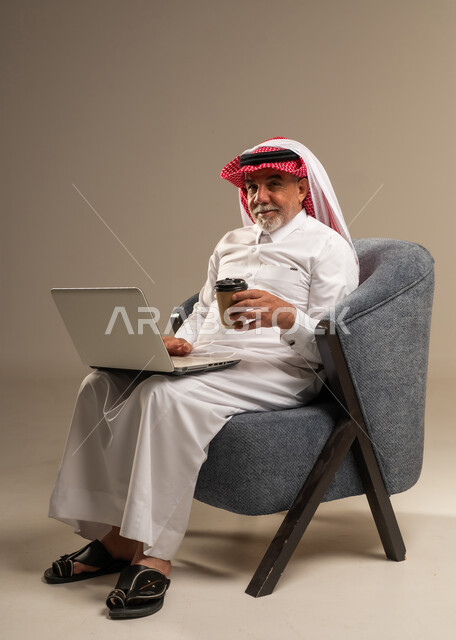 رجل سعودي يستخدم المحمول ويحمل كوب قهوة