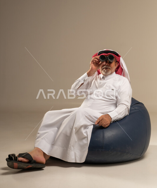 رجل سعودي مسن يحمل منظاراً ويجلس على مقعد محشو