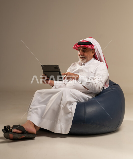 Senior Saudi Man Using Tablet on Blue Bean Bag