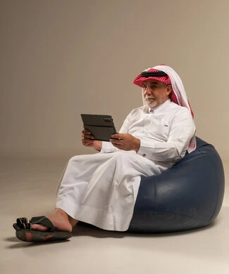 رجل سعودي يستخدم جهاز لوحي يجلس على كرسي استرخاء