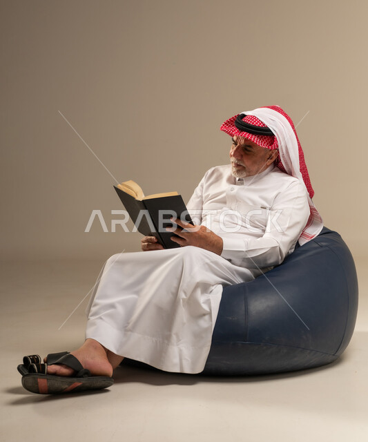Saudi Senior Man Reading Book on Bean Bag chair