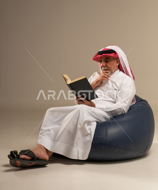Elderly Saudi Man Reading Book on Blue Bean Bag