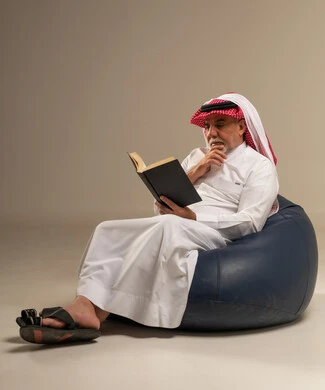 Elderly Saudi Man Reading Book on Blue Bean Bag