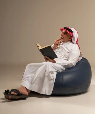 رجل سعودي يقرأ كتاباً على كرسي مريح في استوديو