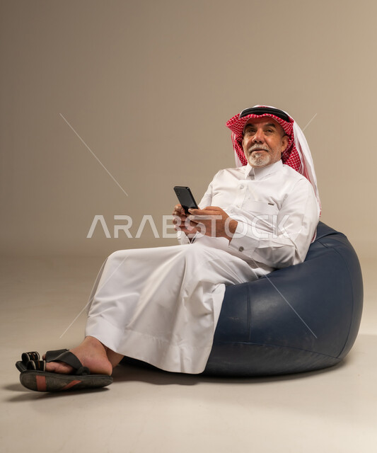 Senior Saudi Man Using Smartphone on Bean Bag
