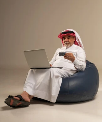 رجل سعودي مسن يستخدم الكمبيوتر المحمول وبطاقة الائتمان