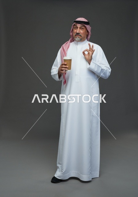 رجل  عربي سعودي خليجي مسن يرتدي الزي الثوب الابيض والشماغ ويحمل فنجان قهوة,  ايماءات واشارات مختلفه , كامل الجسم, خلفيه رماديه