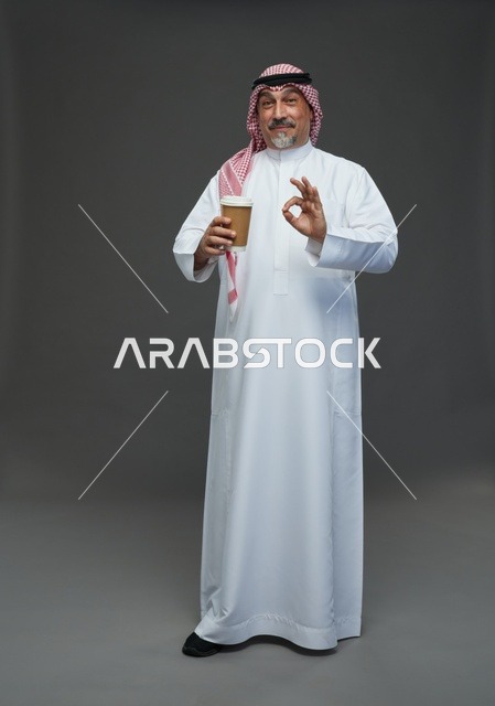رجل  عربي سعودي خليجي مسن يرتدي الزي الثوب الابيض والشماغ ويحمل فنجان قهوة,  ايماءات واشارات مختلفه , كامل الجسم, خلفيه رماديه