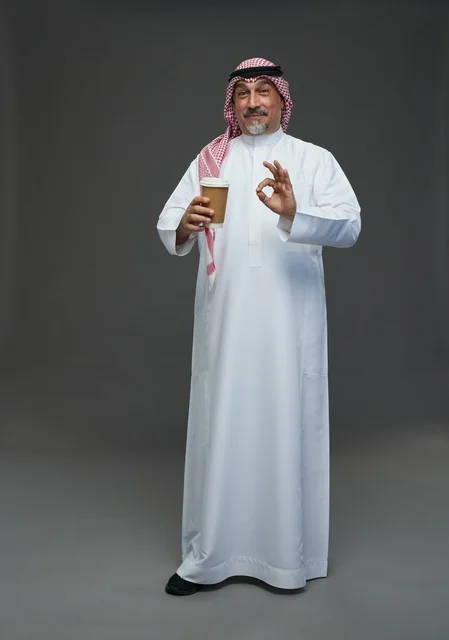 An elderly Arab Saudi Gulf man wearing a white thobe and a shemagh, holding a cup of coffee, with various gestures and signs, full body, gray background.