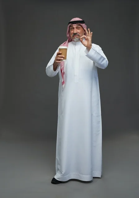 An elderly Arab Saudi Gulf man wearing a white thobe and a shemagh, holding a cup of coffee, with various gestures and signs, full body, gray background.