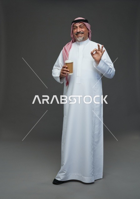 رجل  عربي سعودي خليجي مسن يرتدي الزي الثوب الابيض والشماغ ويحمل فنجان قهوة,  ايماءات واشارات مختلفه , كامل الجسم, خلفيه رماديه