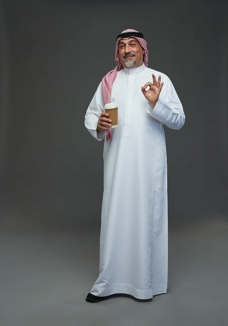 An elderly Arab Saudi Gulf man wearing a white thobe and a shemagh, holding a cup of coffee, with various gestures and signs, full body, gray background.