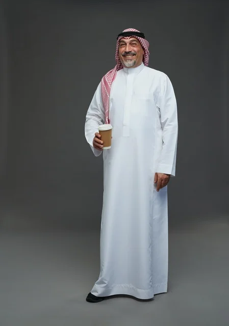 رجل  عربي سعودي خليجي مسن يرتدي الزي الثوب الابيض والشماغ ويحمل فنجان قهوة,  ايماءات واشارات مختلفه , كامل الجسم, خلفيه رماديه