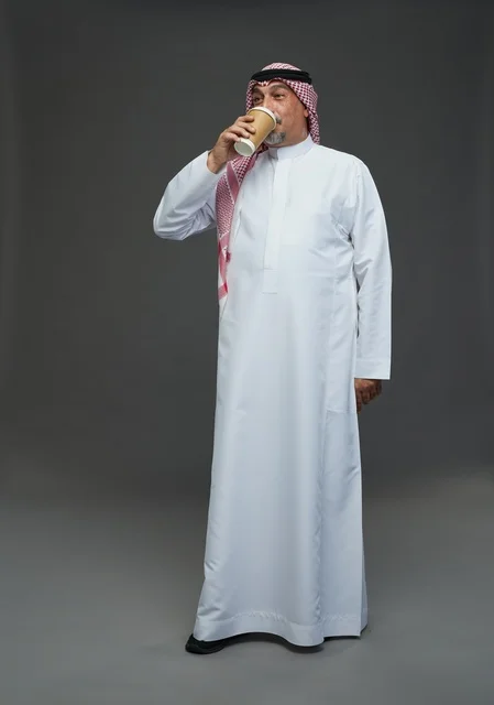 رجل  عربي سعودي خليجي مسن يرتدي الزي الثوب الابيض والشماغ ويحمل فنجان قهوة,  ايماءات واشارات مختلفه , كامل الجسم, خلفيه رماديه